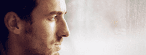 A closeup of a sad man looking longingly out a window on a rainy day